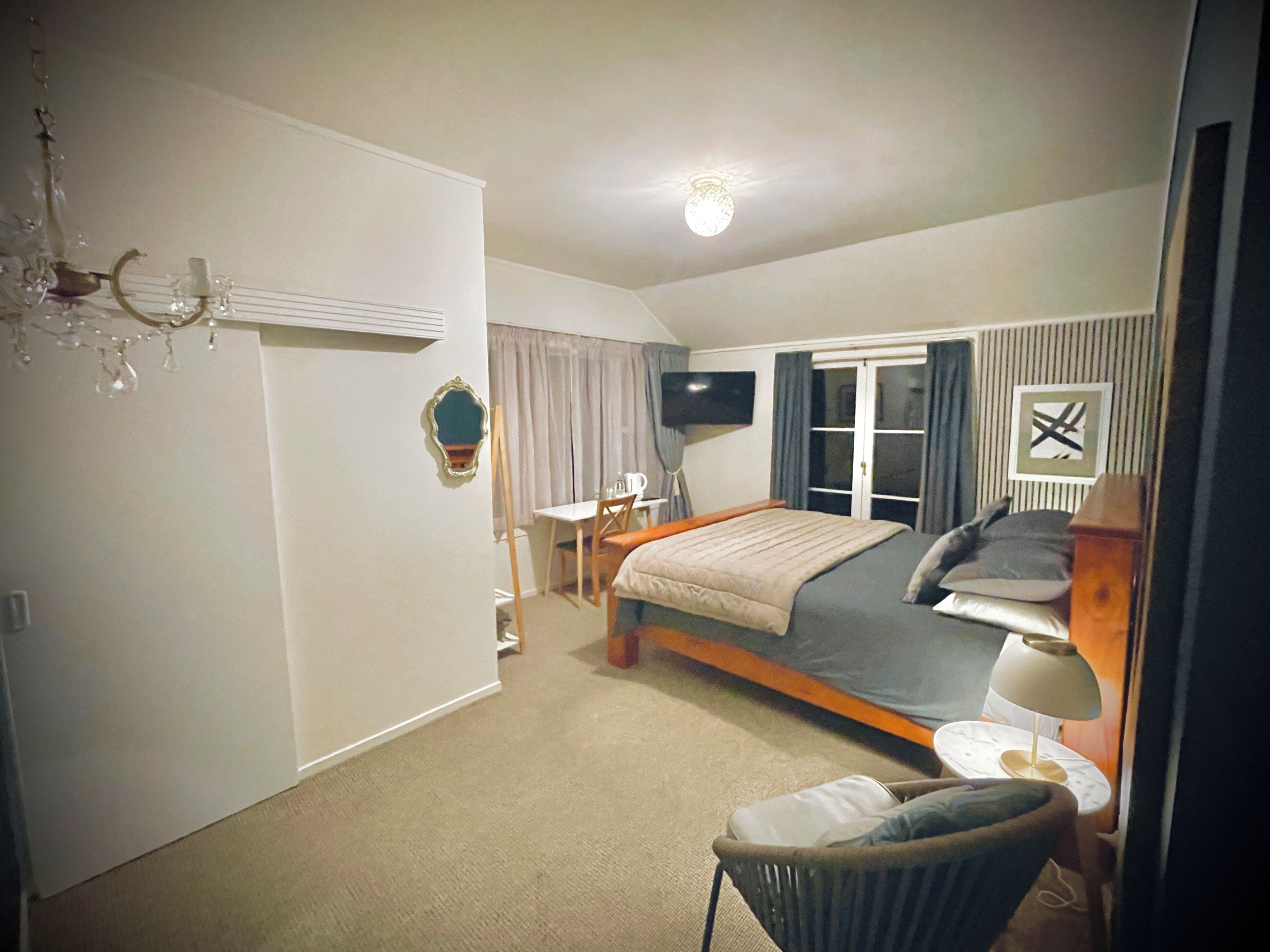 Une chambre d’hôtel avec un lit, une chaise, un bureau, un téléviseur et un lustre.