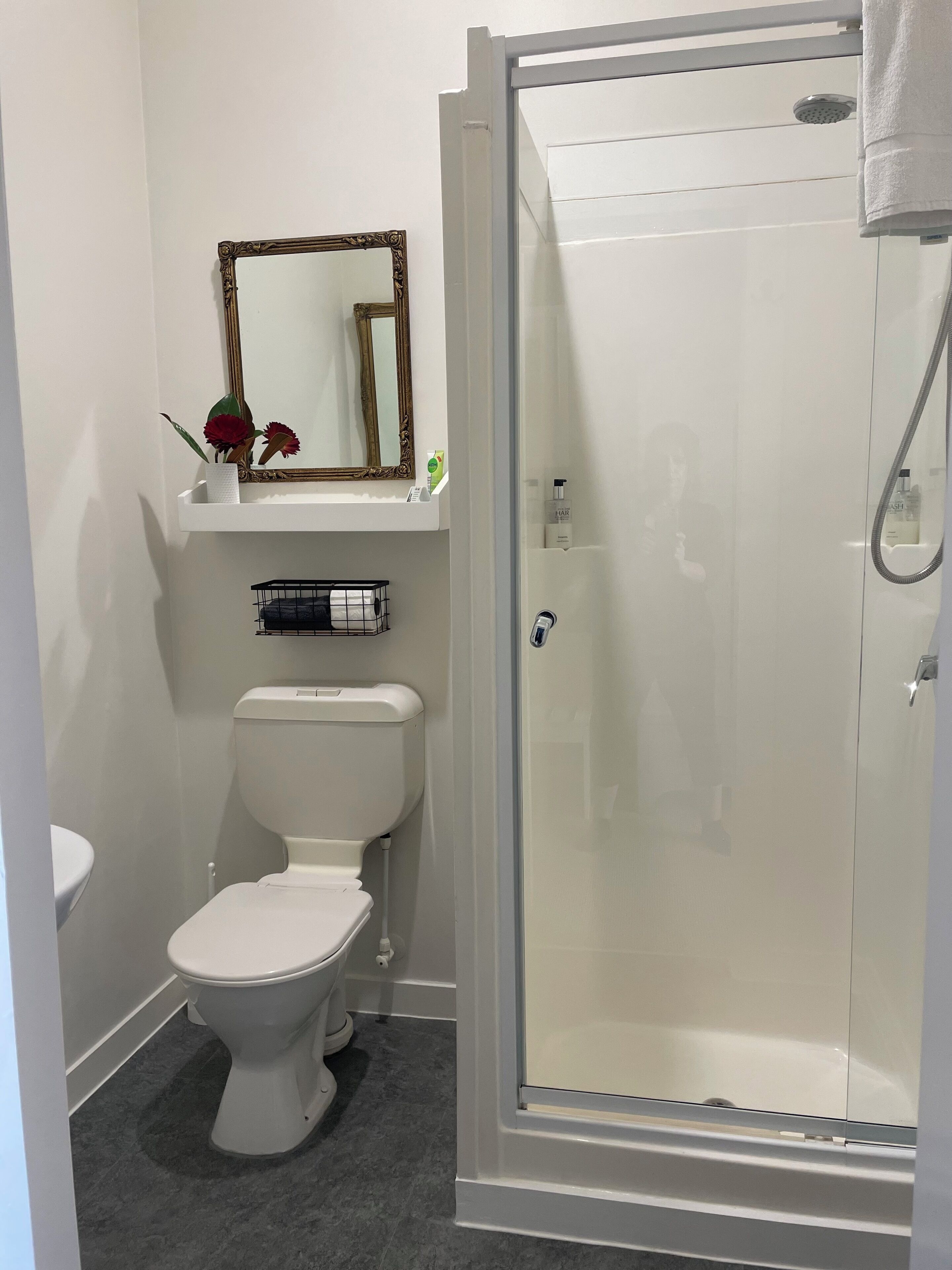 Baño con inodoro, cabina de ducha, espejo y repisas con artículos de aseo.