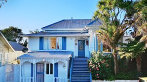 A two-story house with a blue roof and white walls, a front porch with a white railing, and a staircase leading to the front door. - Bavaria Boutique Hotel (Auckland)