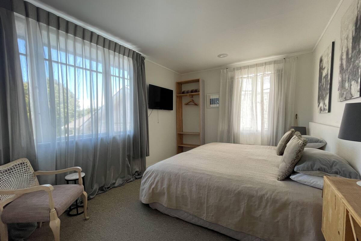 Una habitación de hotel con una cama grande, una silla, un televisor montado en la pared y un armario.