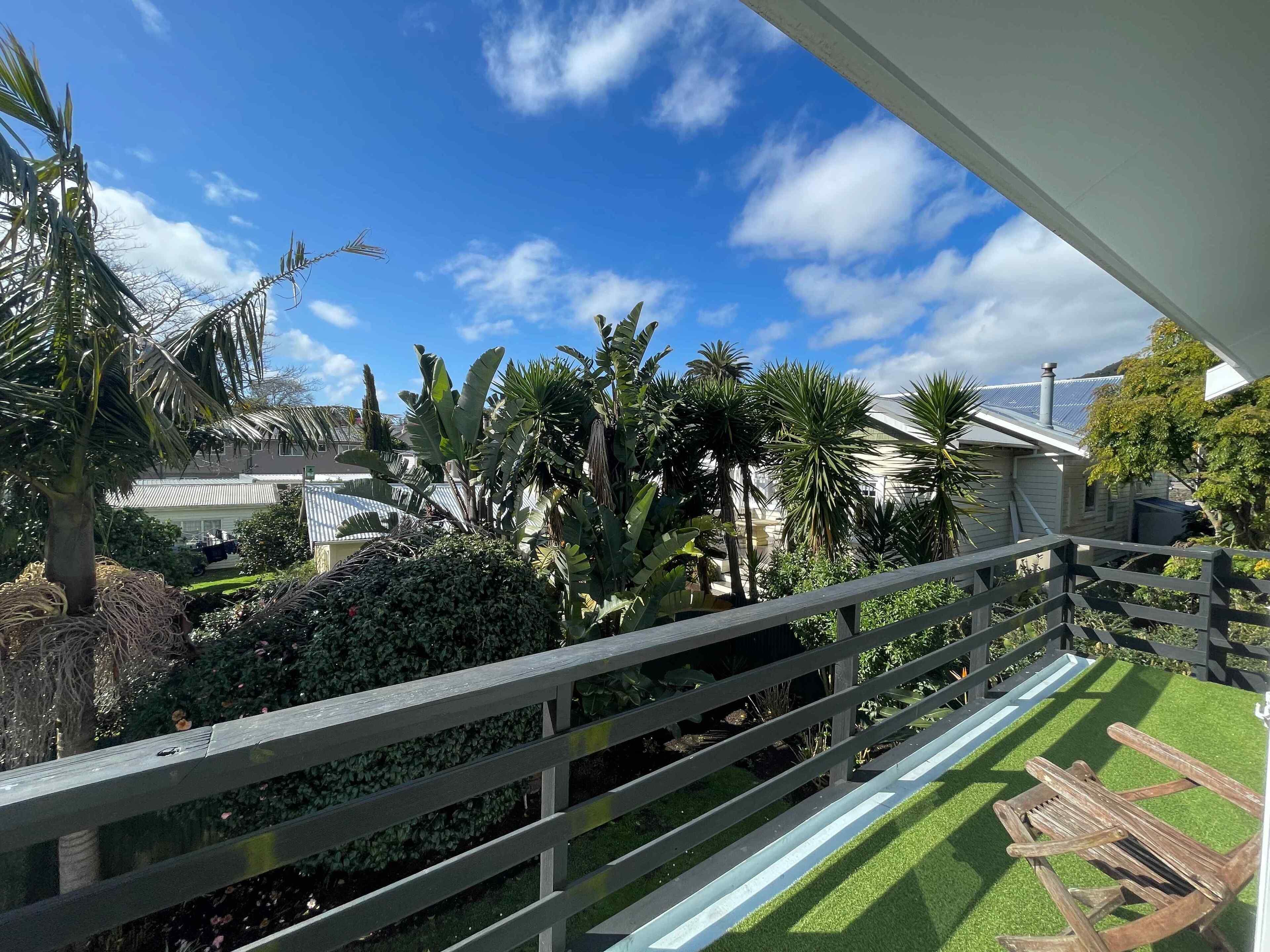 A balcony with a view of a garden, a house, and a clear blue sky.