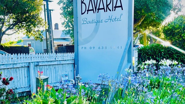 A sign for Bavaria Boutique Hotel with the number 83, surrounded by lush greenery and flowers. - Bavaria Boutique Hotel (Auckland)