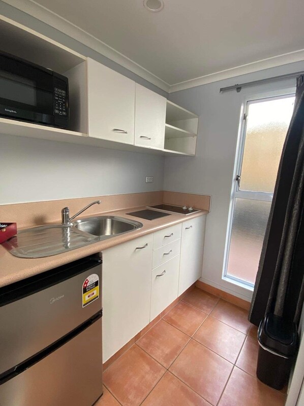 Una cocina compacta equipada con microondas, pileta y alacenas.