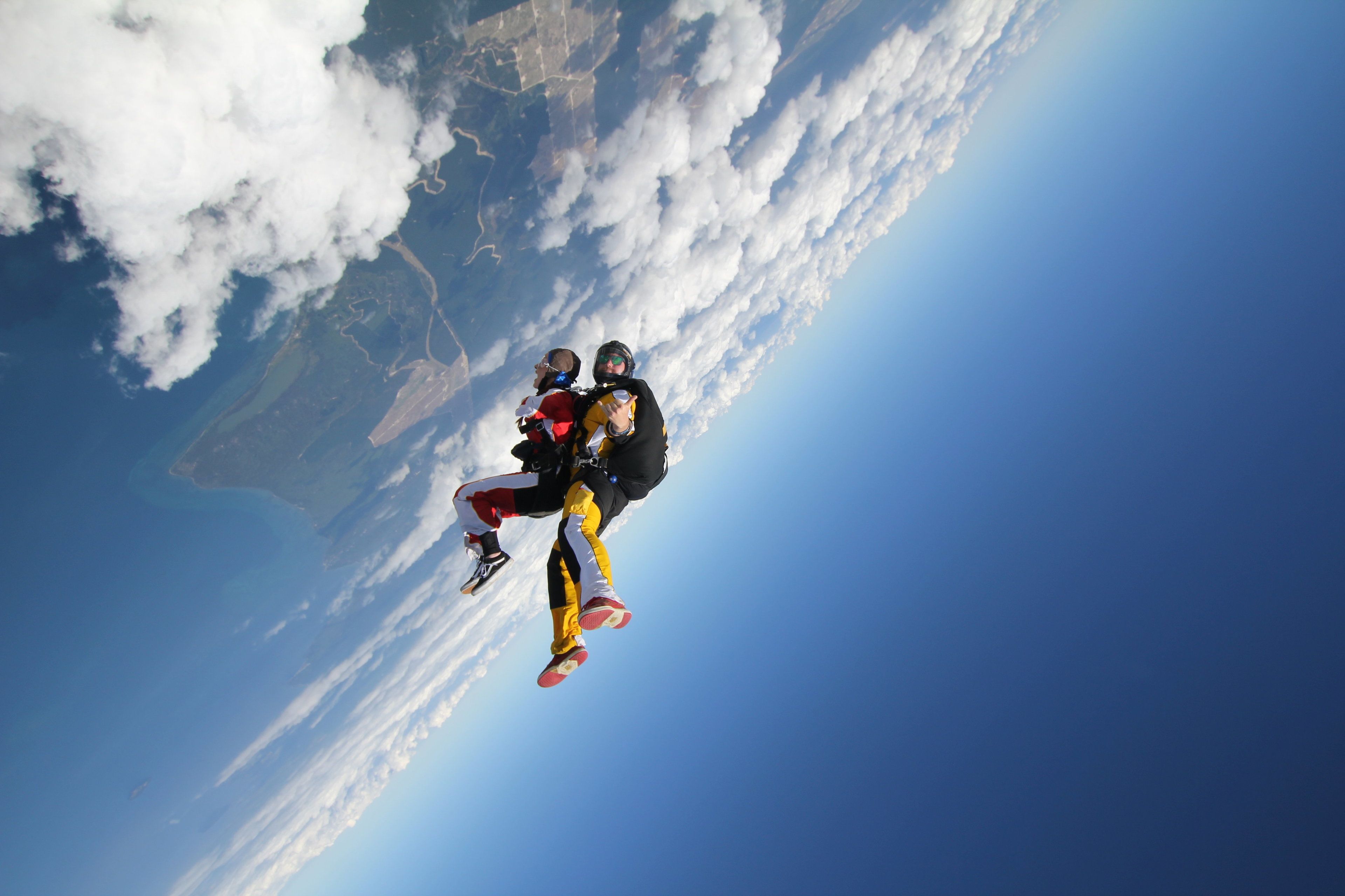 A person skydiving with a parachute, with a view of clouds and a landscape below.
