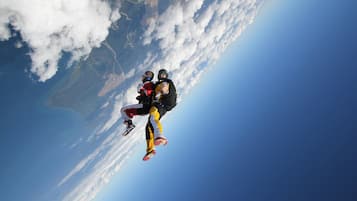 A person skydiving with a parachute, with a view of clouds and a landscape below.
