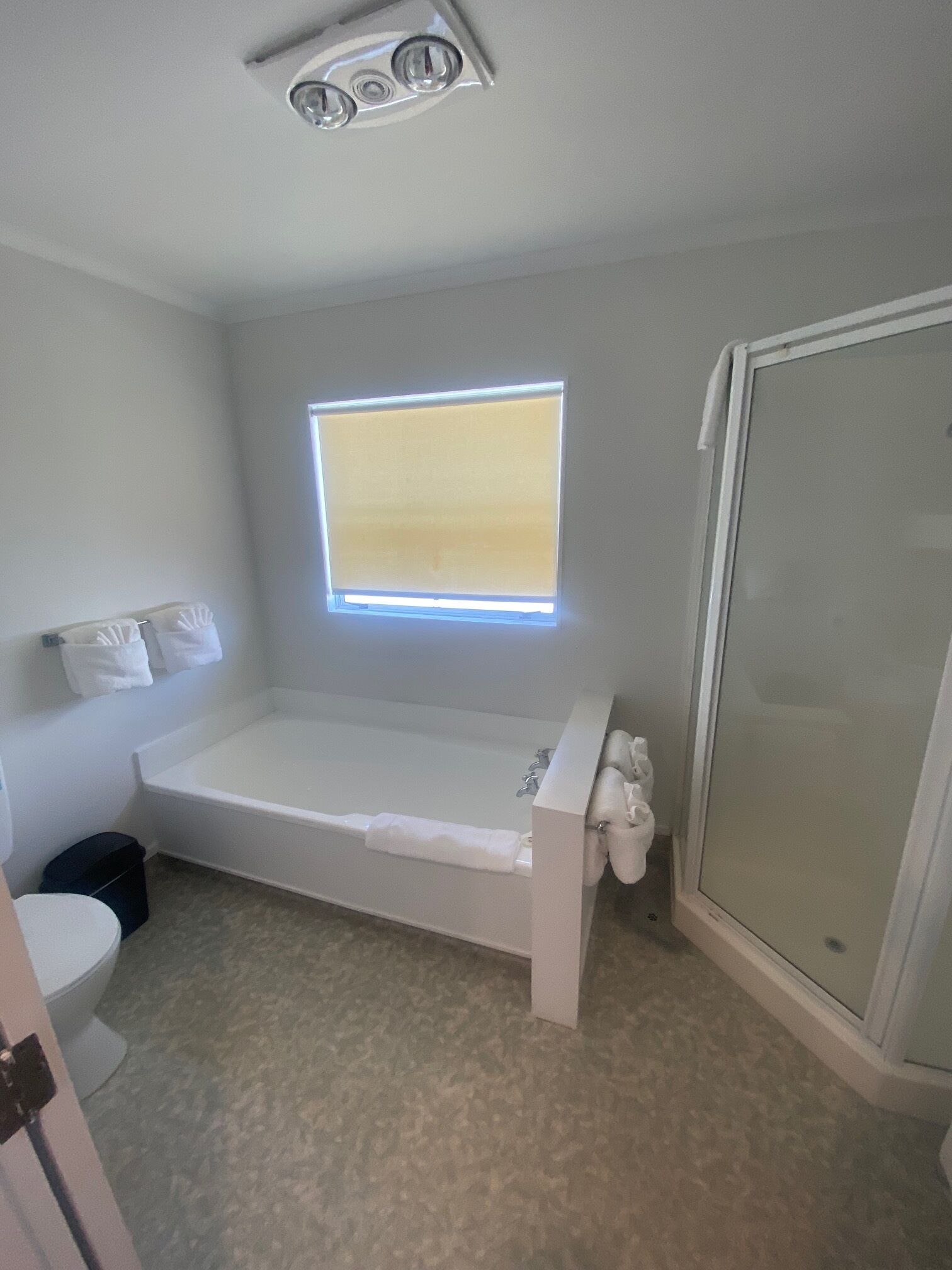Un baño con bañera, inodoro, ventana con persianas y zona de ducha.