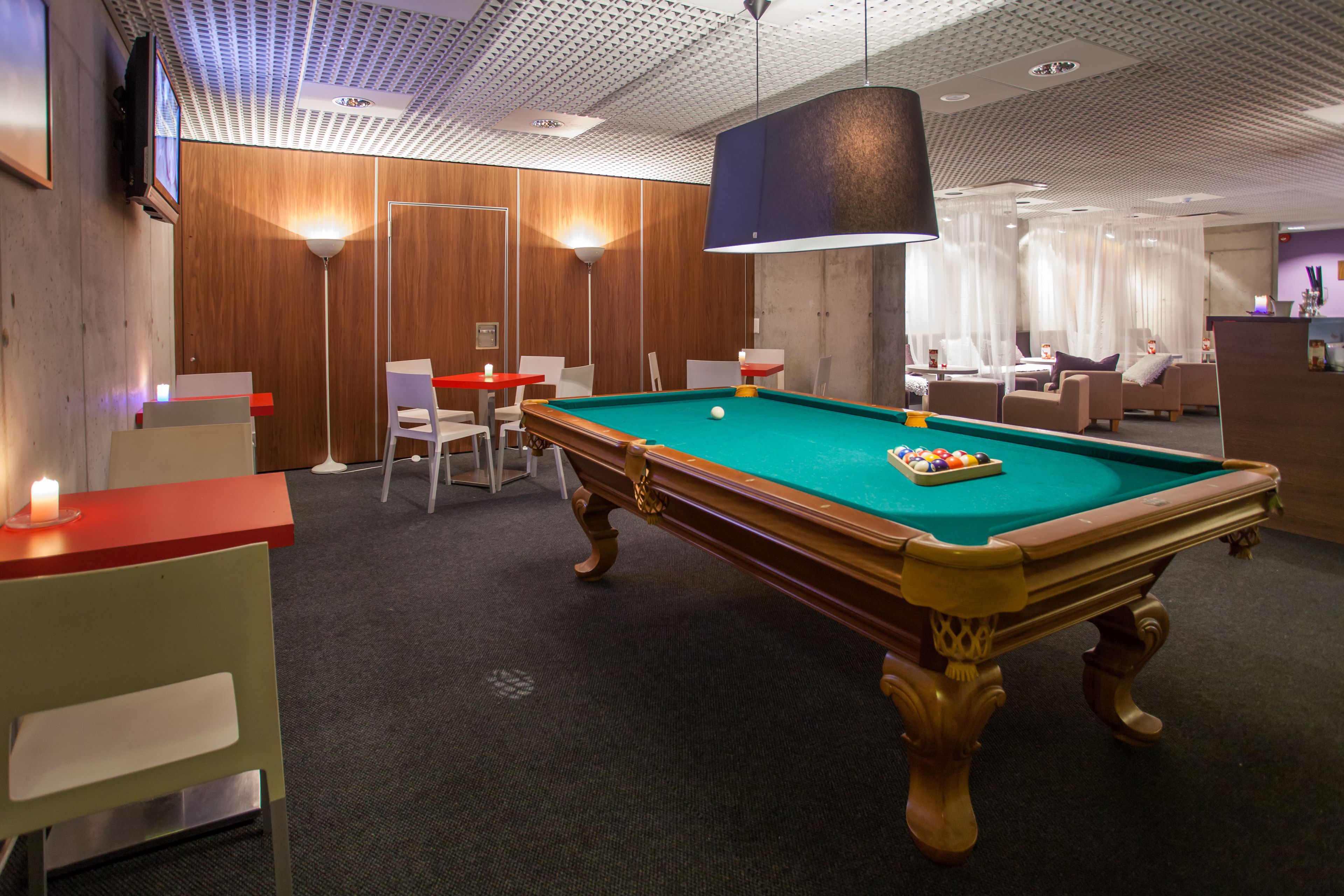 Una mesa de billar en una sala con paneles de madera, una zona de bar y un área de descanso con sillas y un sofá.