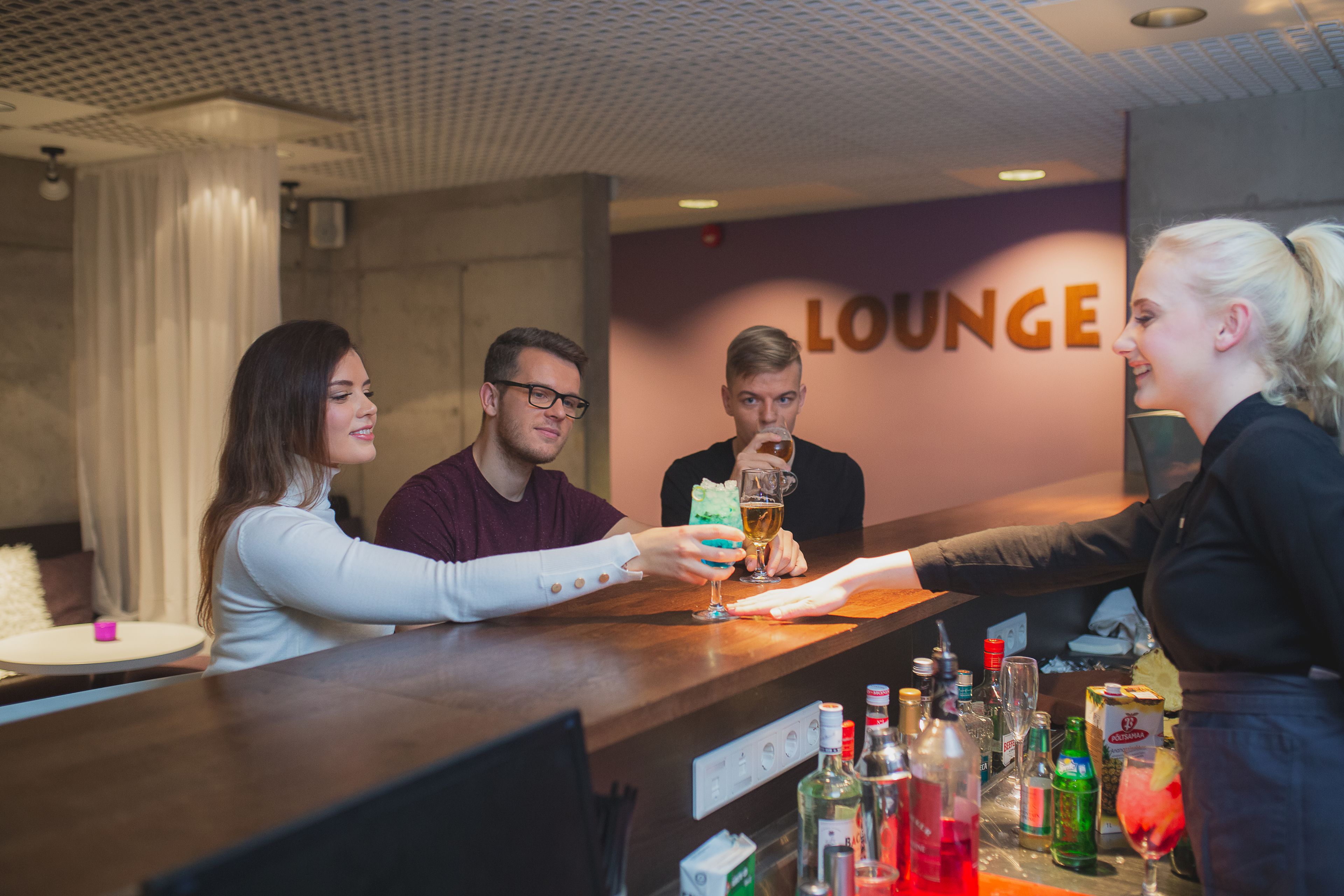 A bar area with a counter, a person serving drinks, and a wall with the word "LOUNGE".