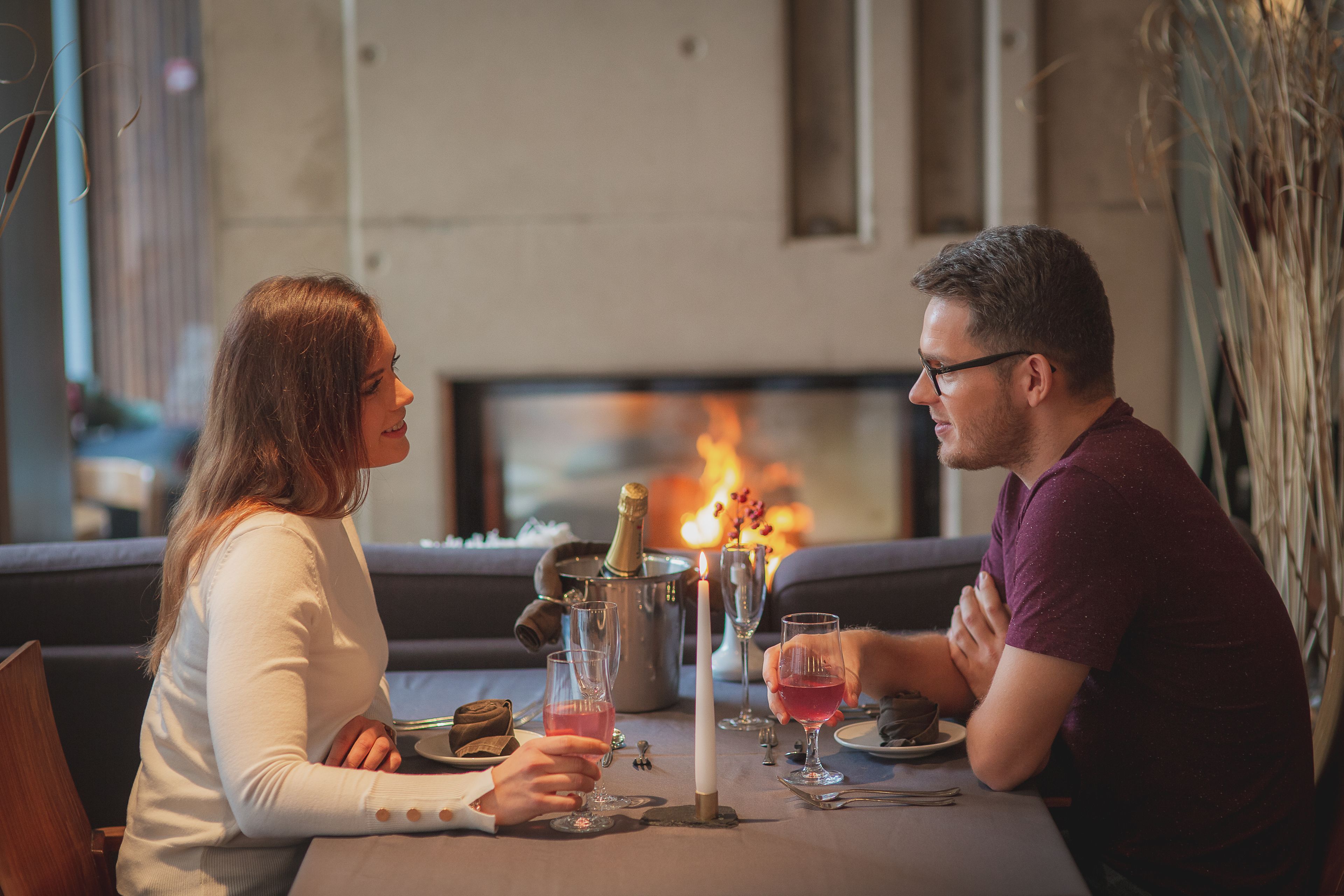 A couple dining at a table with a fireplace in the background.