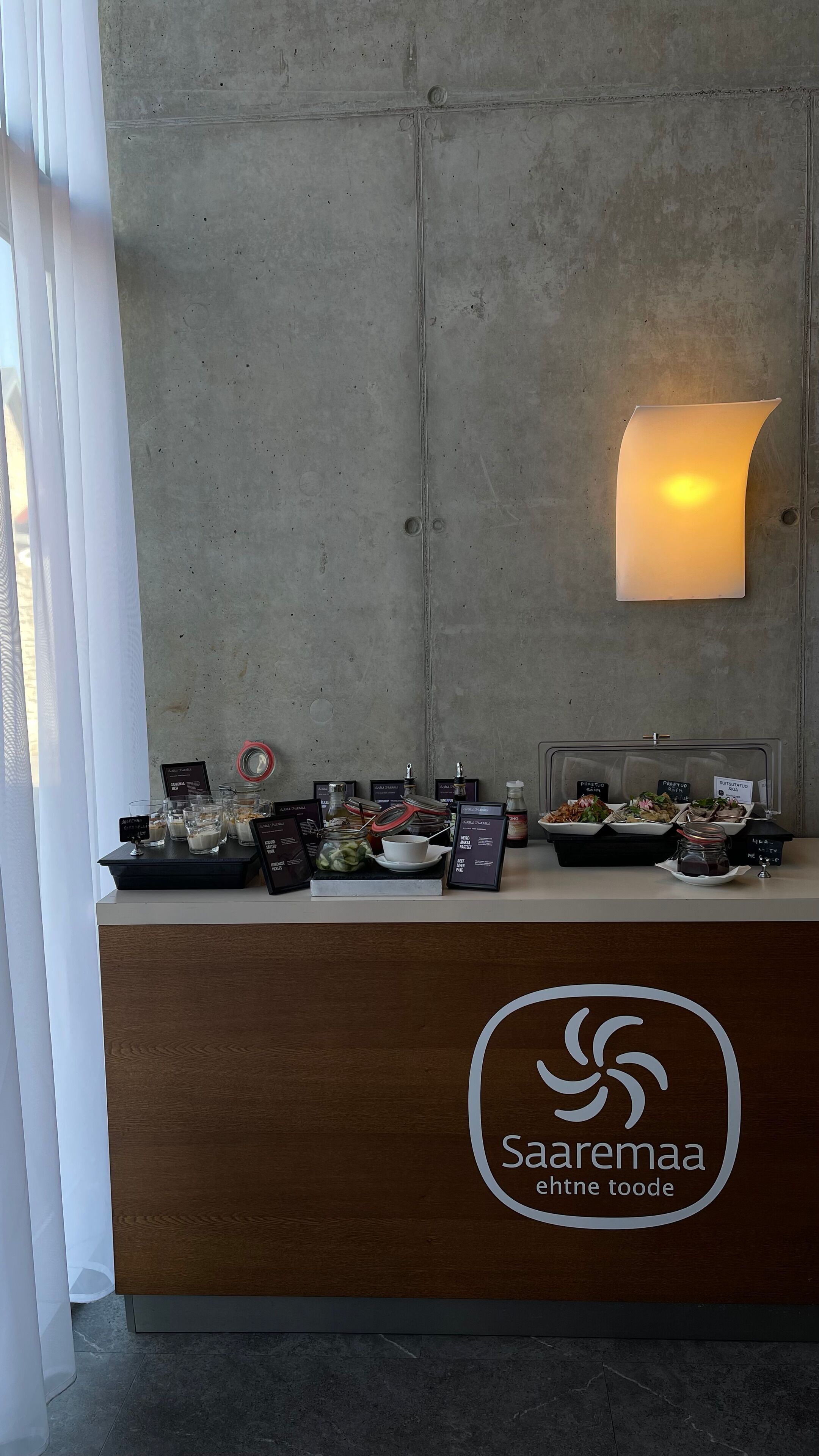 Una mesa de recepción con un logotipo, una lámpara fijada a la pared y una exhibición de alimentos.