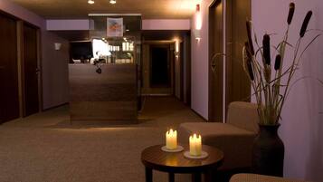 A hotel lobby with a reception desk, a seating area with two chairs and a table, and a vase with plants.