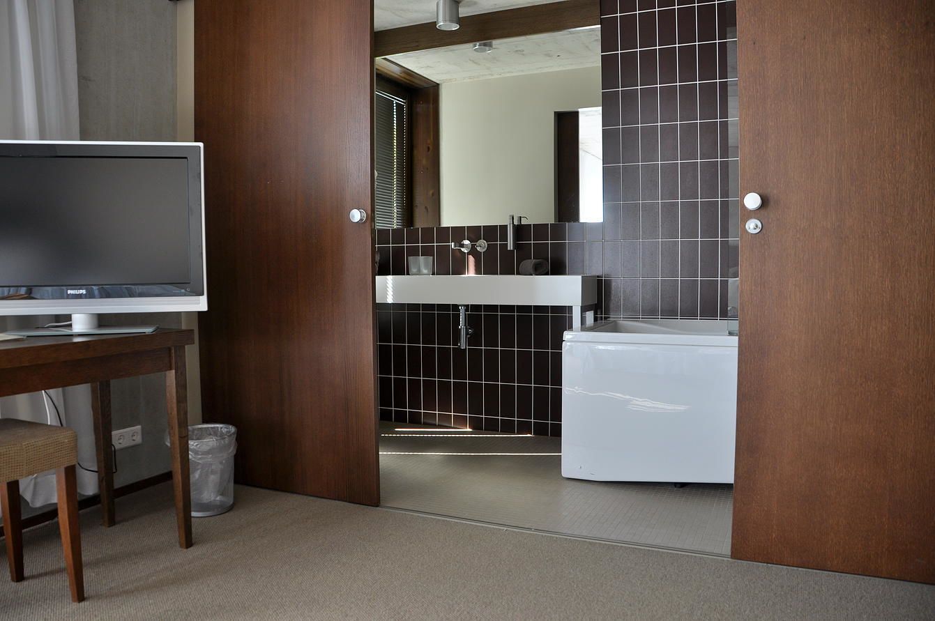 A modern bathroom with a white sink, dark tiled walls, and a wooden door.