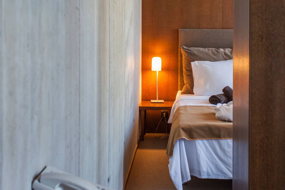 A hotel room with a bed, bedside lamp, and a telephone on the nightstand.