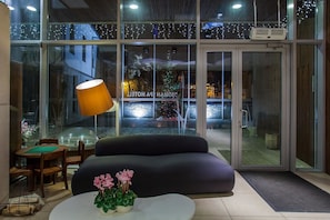 A modern hotel lobby with a seating area, a glass door entrance, and a Christmas tree visible through the glass.