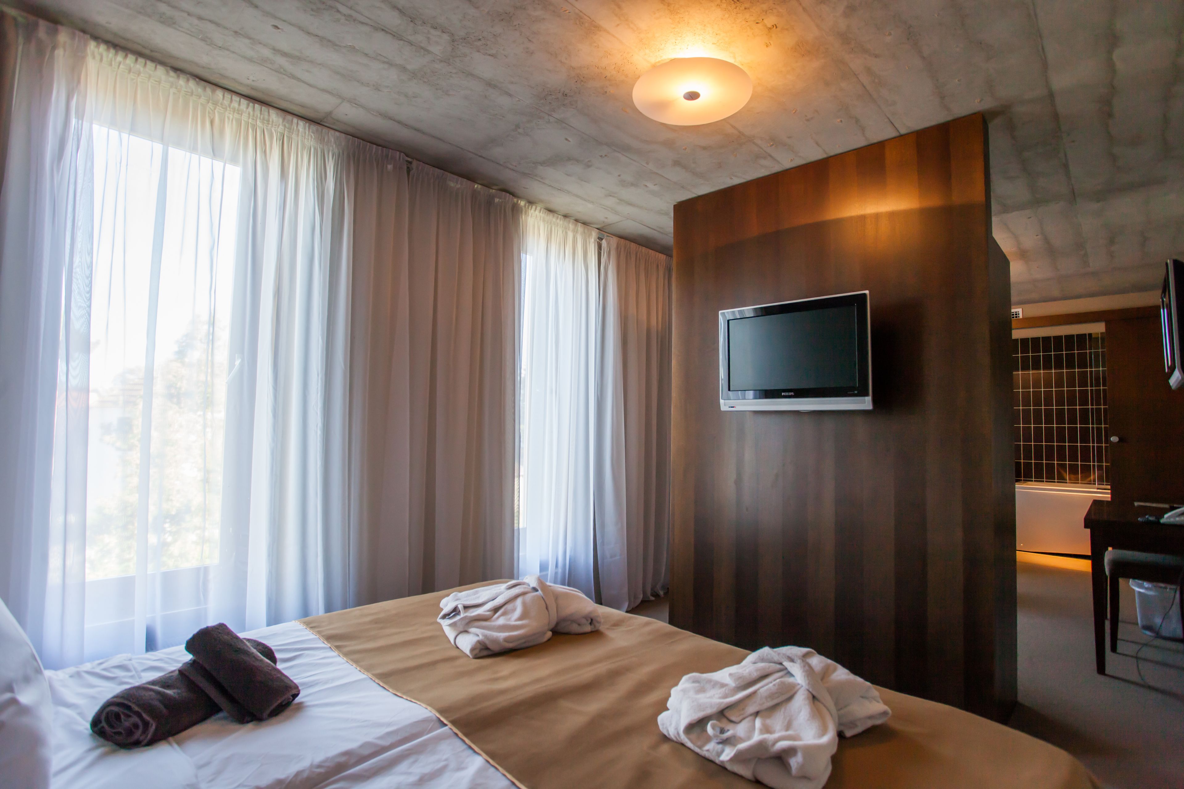 A hotel room with a bed, a TV mounted on the wall, and a window with curtains.
