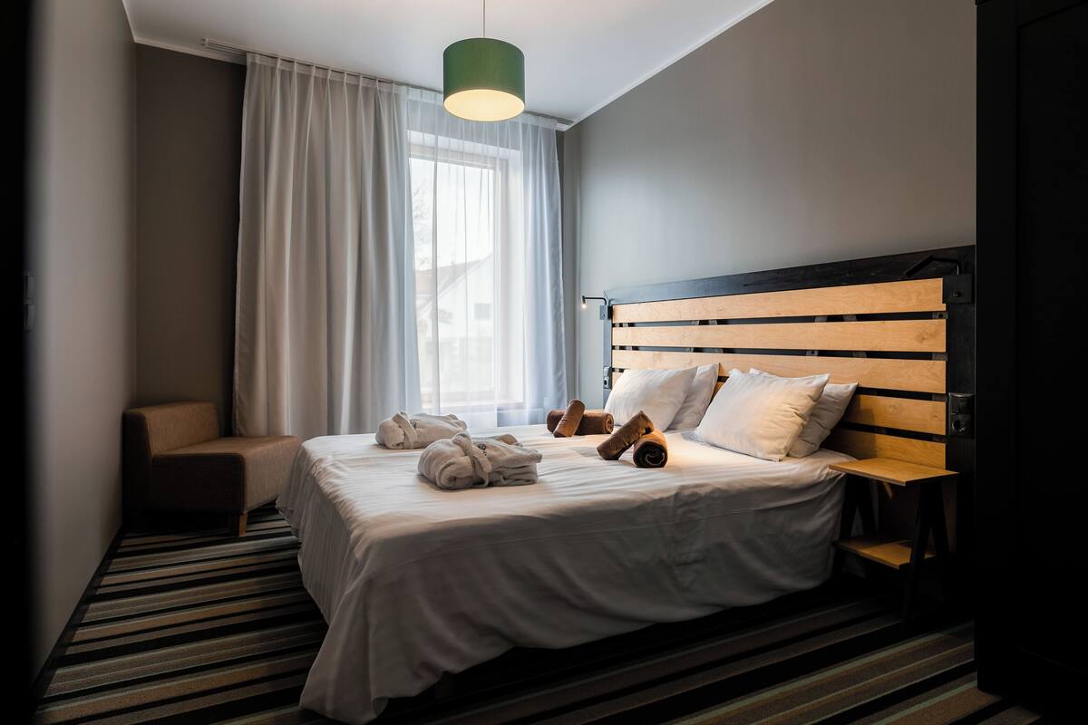 A hotel room with a bed, a chair, a nightstand, and a window with curtains.