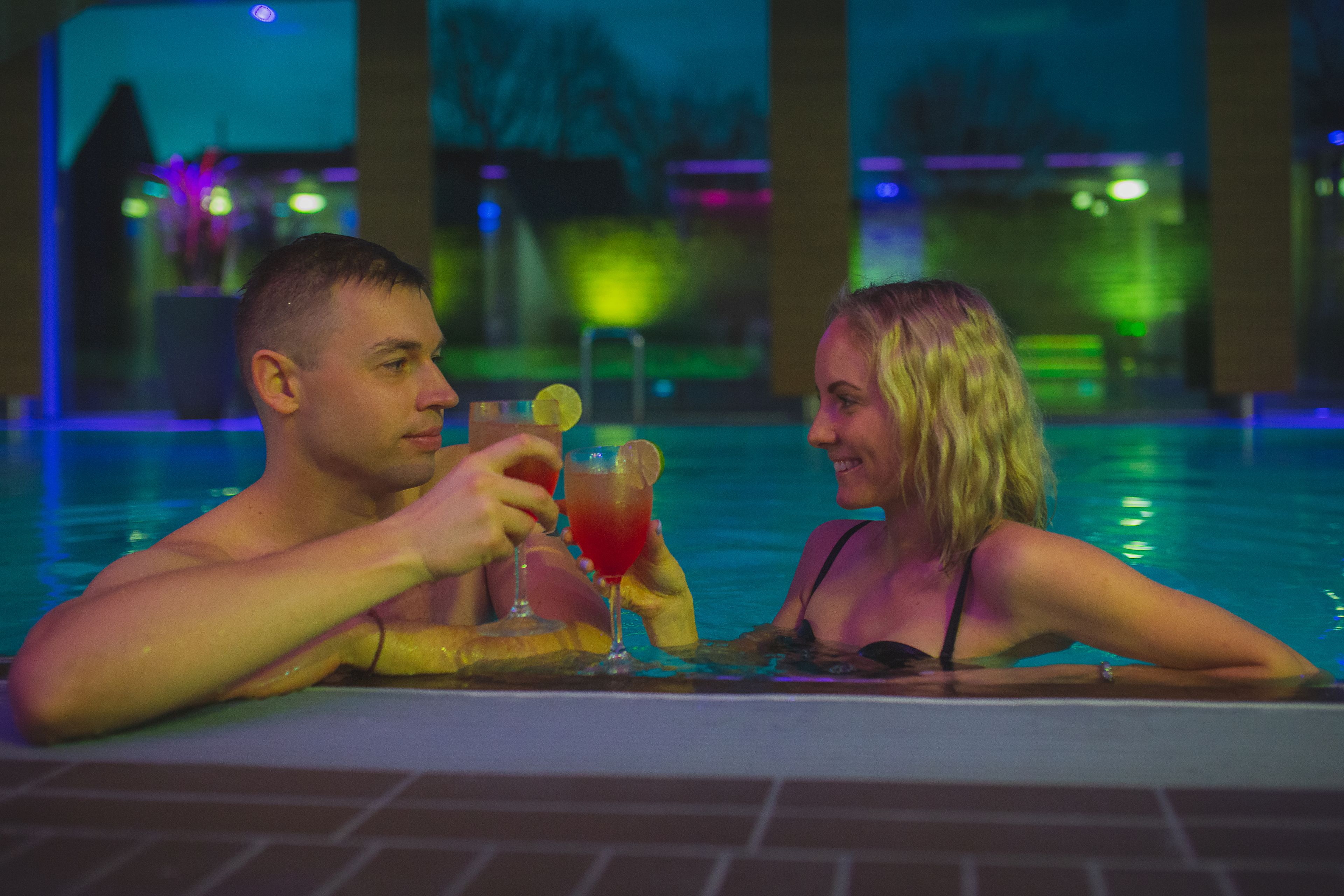 Two people in a pool with a drink in each hand.