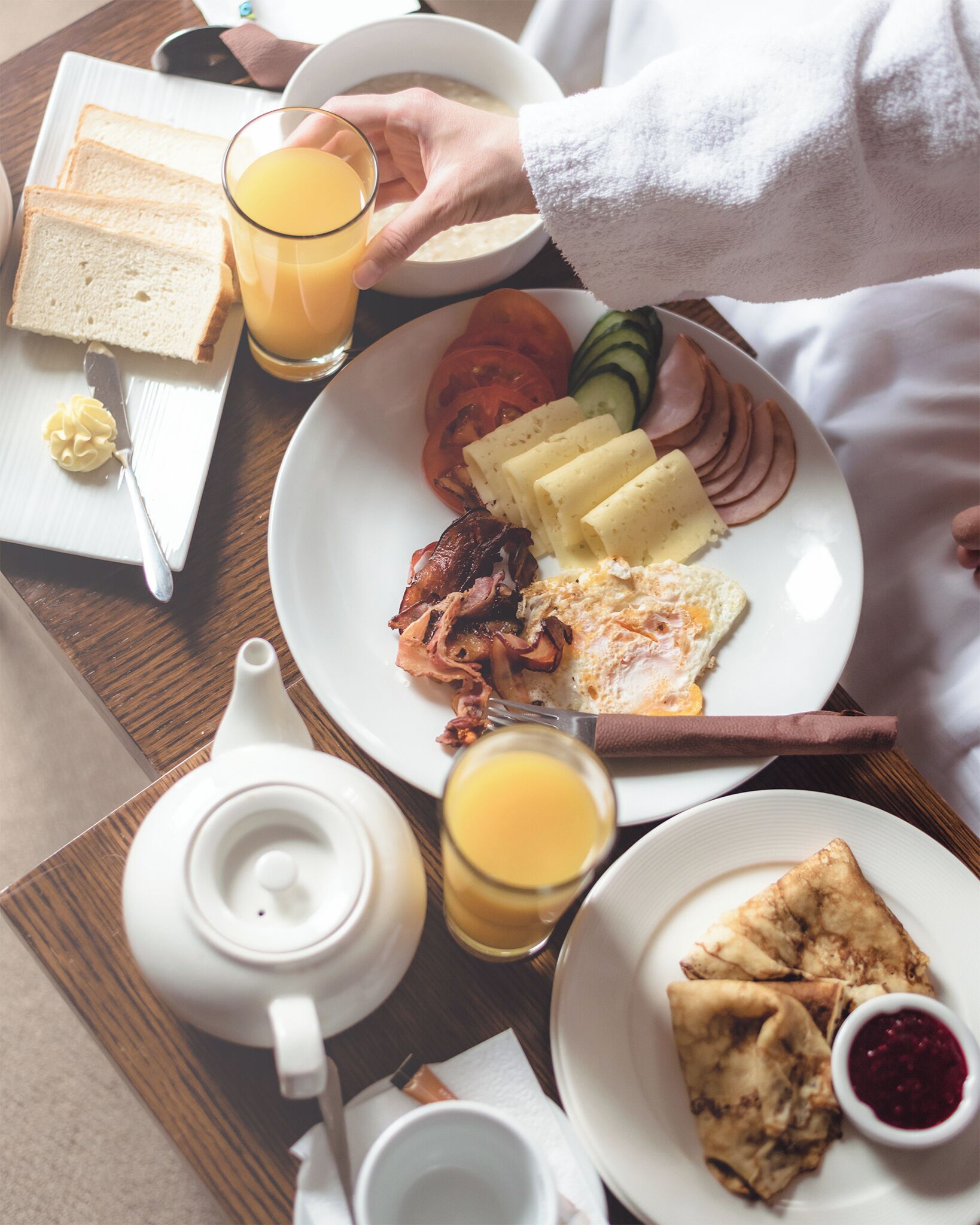 A breakfast tray with toast, eggs, bacon, tomatoes, cucumbers, ham, and a glass of orange juice.