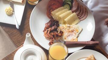 A breakfast tray with toast, eggs, bacon, tomatoes, cucumbers, ham, and a glass of orange juice.