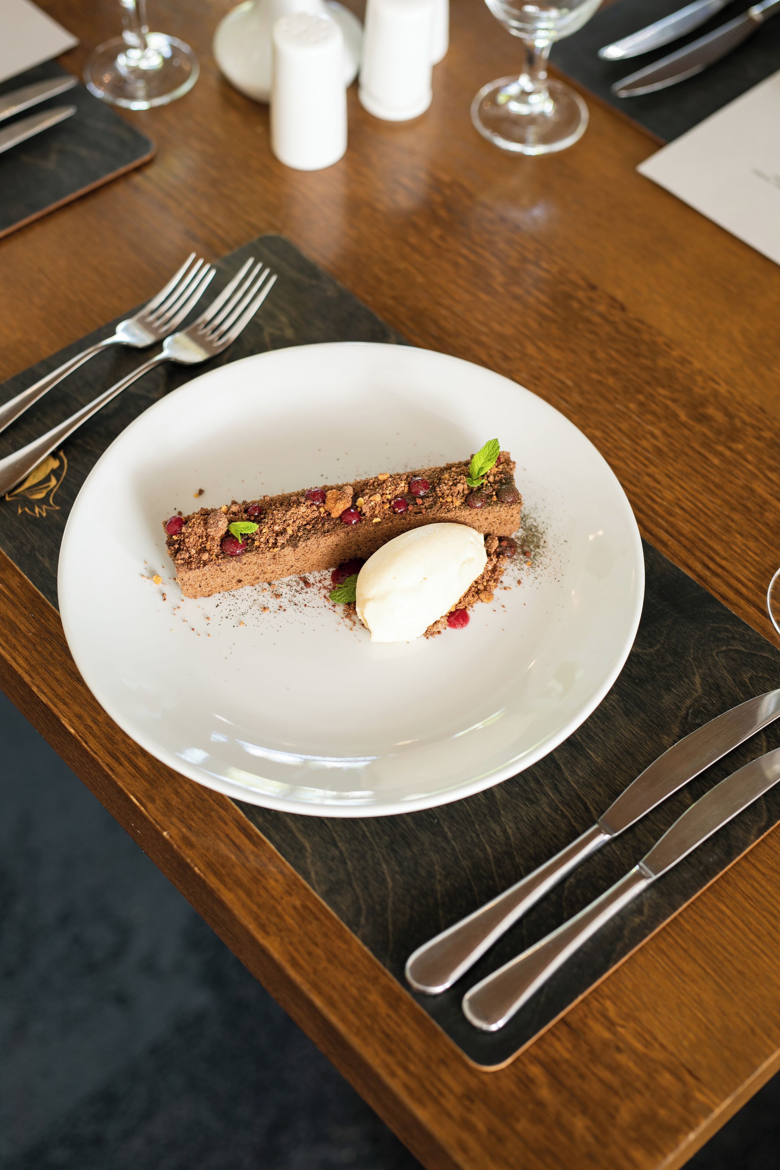 A dessert on a white plate with a wooden table, silverware, and salt and pepper shakers.