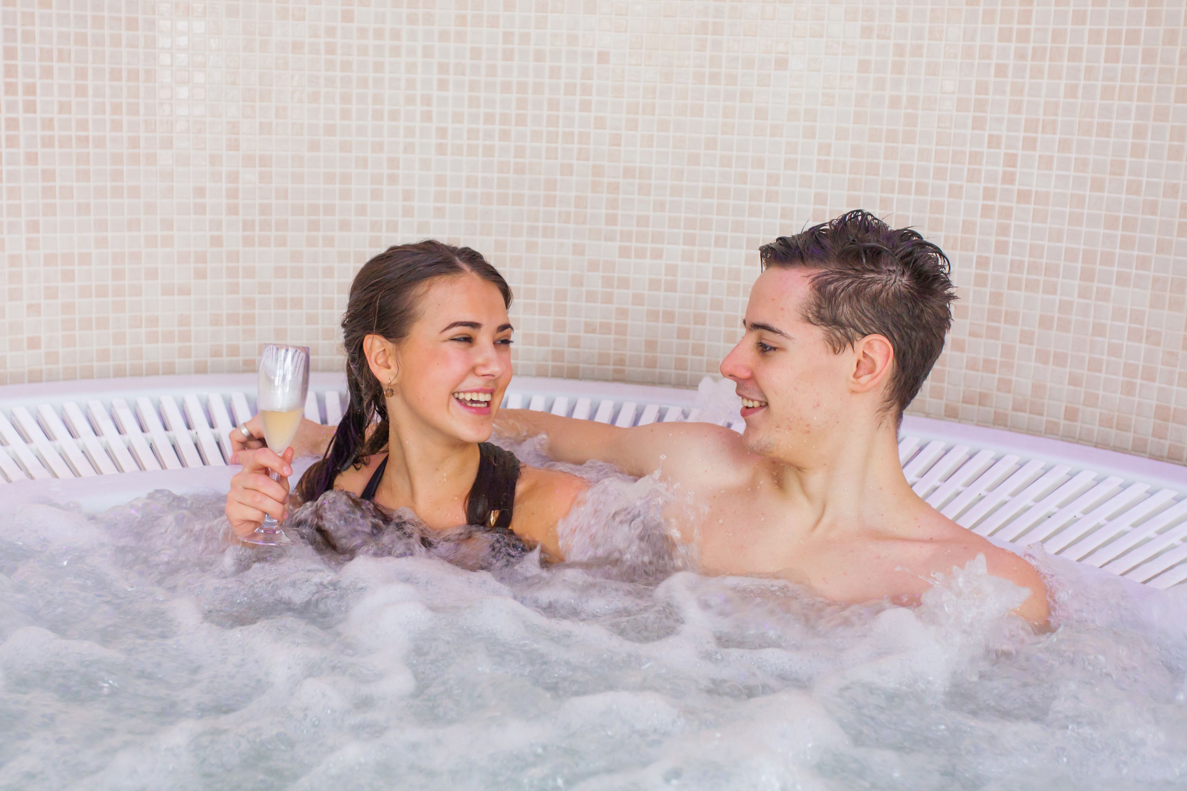 Una pareja en un jacuzzi con una pared de azulejos al fondo.