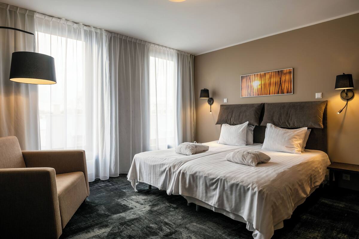A hotel room with a large bed, two bedside lamps, a chair, and a painting on the wall.