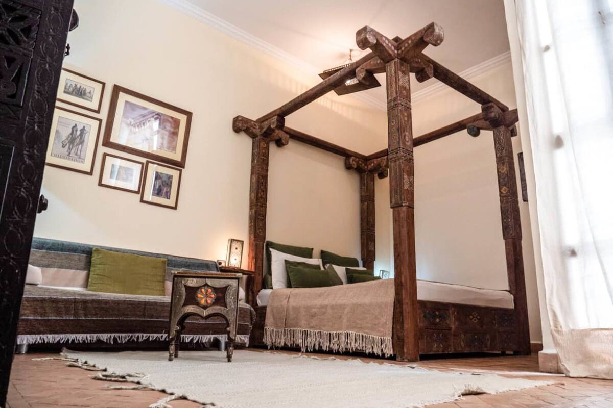 A traditional four-poster bed with a wooden frame, a small wooden nightstand, and a bench with cushions.