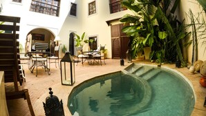A courtyard with a pool, outdoor seating, and lush greenery. - Riad Les Ammonites (Marrakech)
