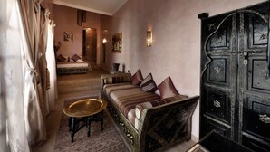A traditional Moroccan room with a sofa, a small table, and a large wooden cabinet. - Riad Les Ammonites (Marrakech)