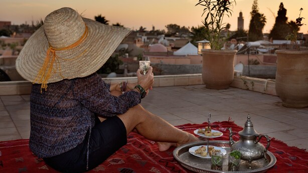 A person sitting on a red mat outdoors with a tray of food and a teapot. - Riad Les Ammonites (Marrakech)
