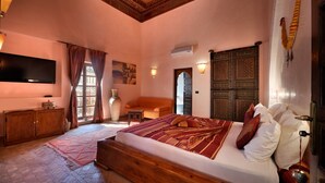 A bedroom with a large bed, wooden headboard, a flat-screen TV, a wooden cabinet, and a decorative wall hanging. - Riad Les Ammonites (Marrakech)