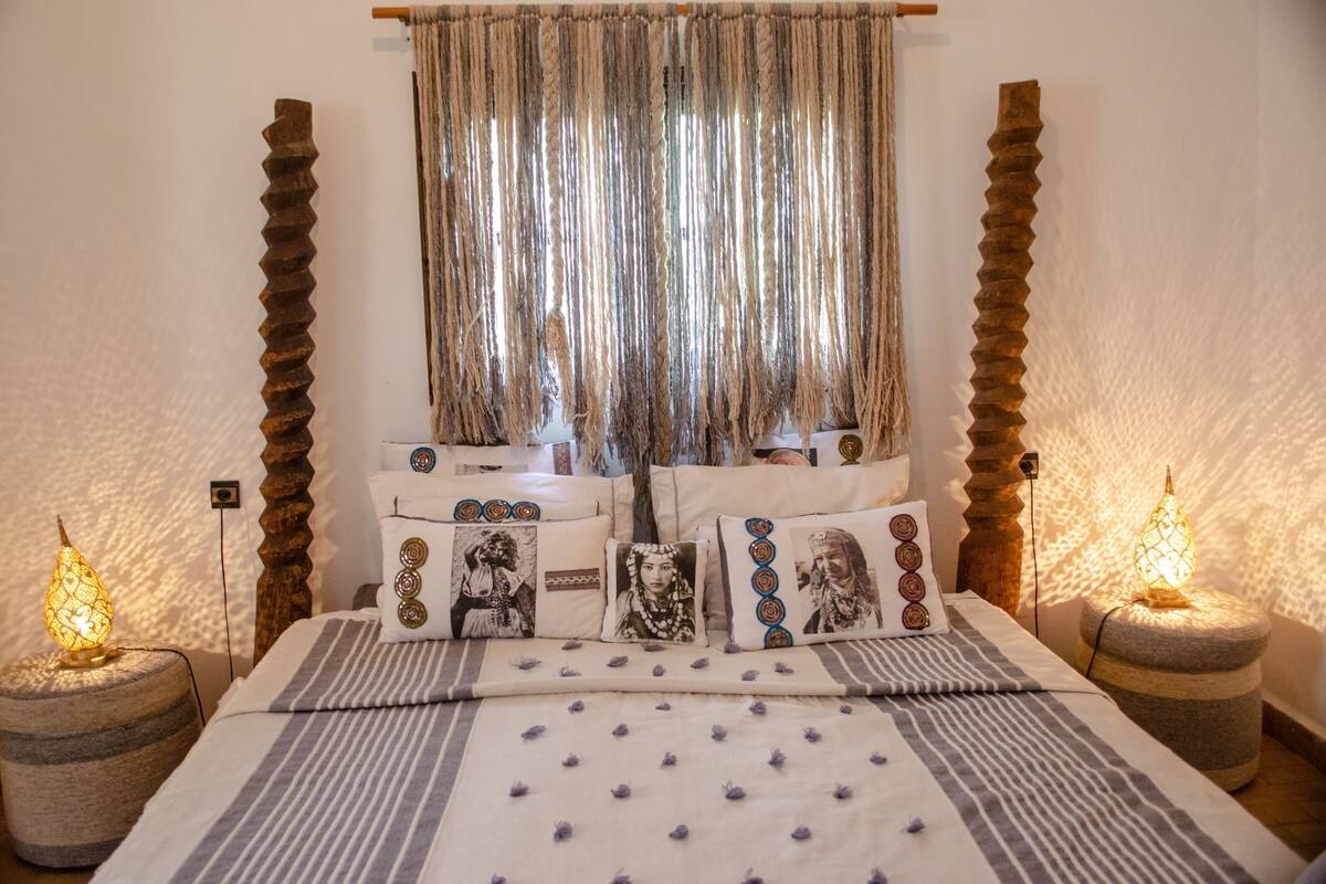 A bed with striped bedding, decorative pillows, and a window with curtains.