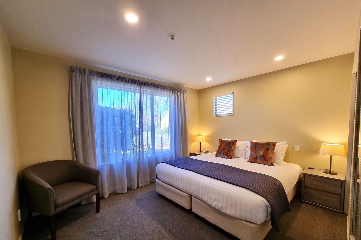 Una habitación de hotel con cama, una silla, una mesita de noche y una ventana con cortinas.