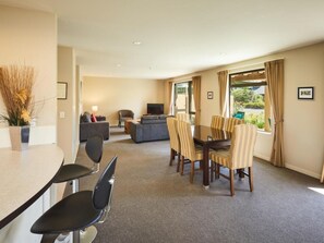 A modern living room with a dining area, a sofa, a TV, and a window with curtains. - Vintner's Retreat (Rapaura)