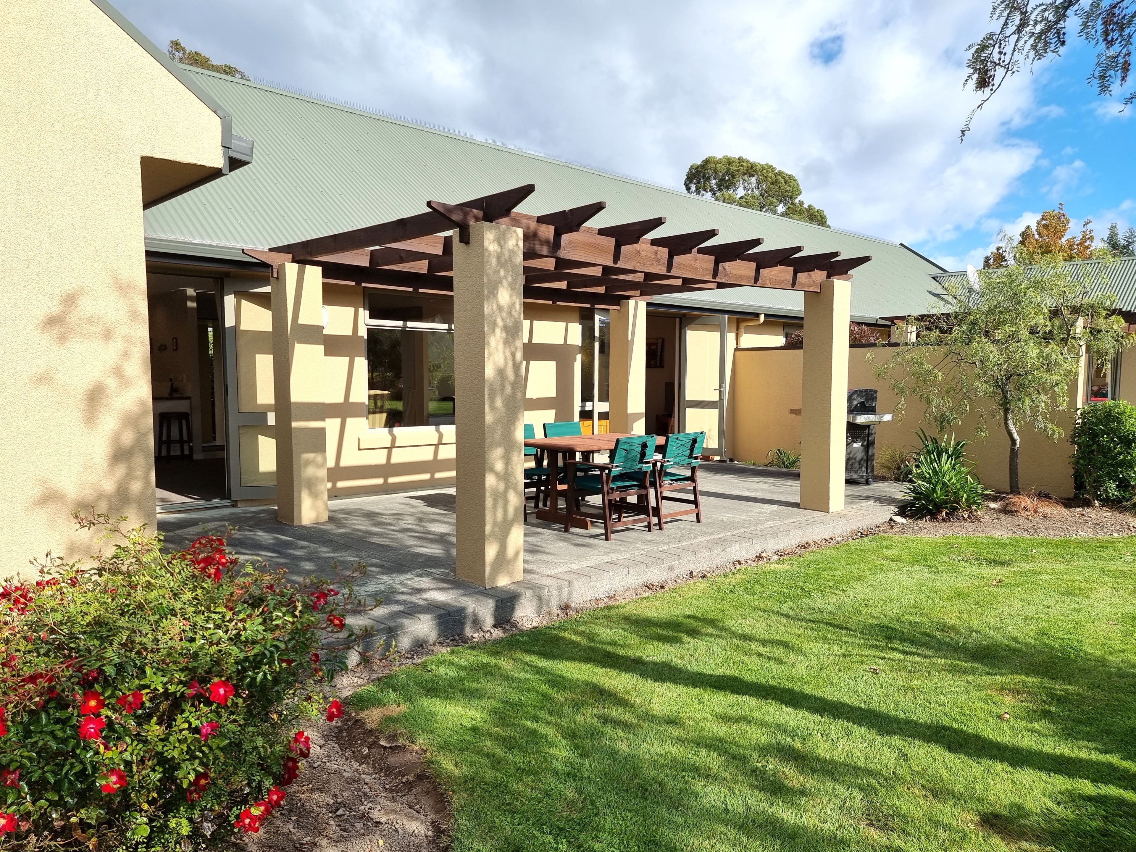 A covered patio area with a table and chairs, a pergola structure, and a lawn with red flowers.
