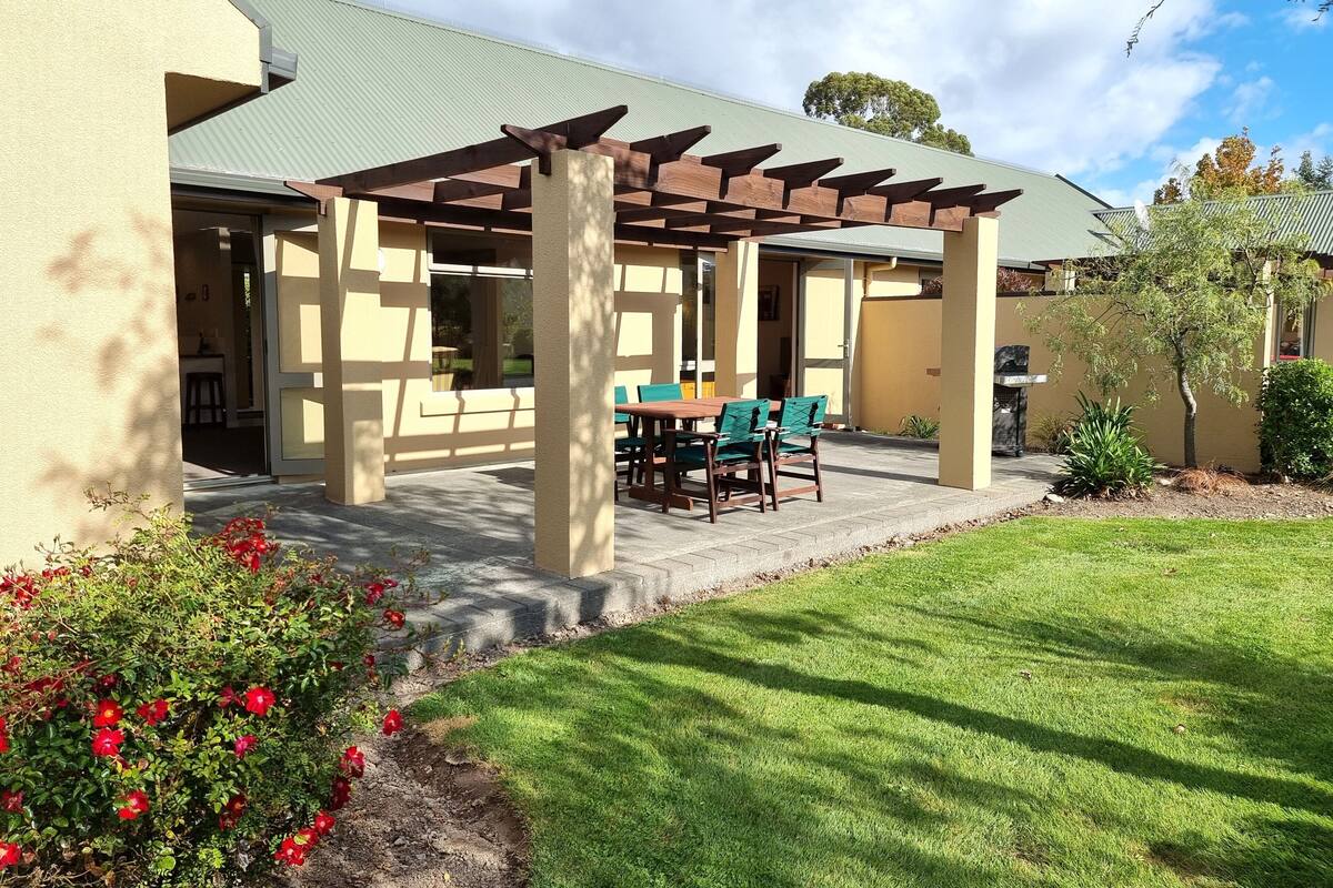 A covered patio area with a table and chairs, a pergola structure, and a well-maintained lawn.