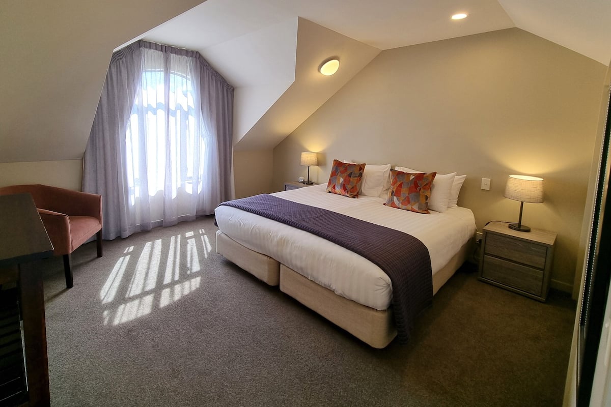 A modern hotel room with a large bed, a desk, and a chair.