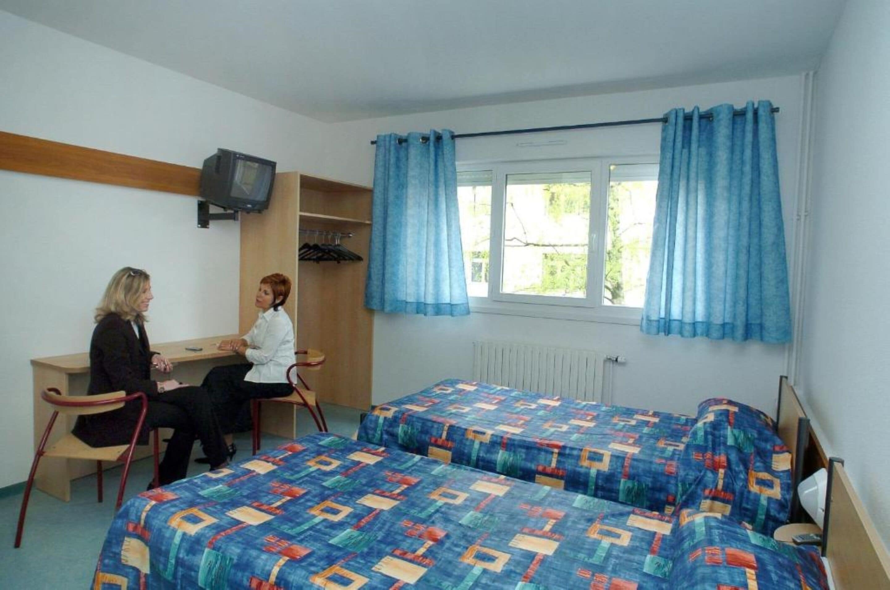 A room with two beds, a desk, a chair, and a television.