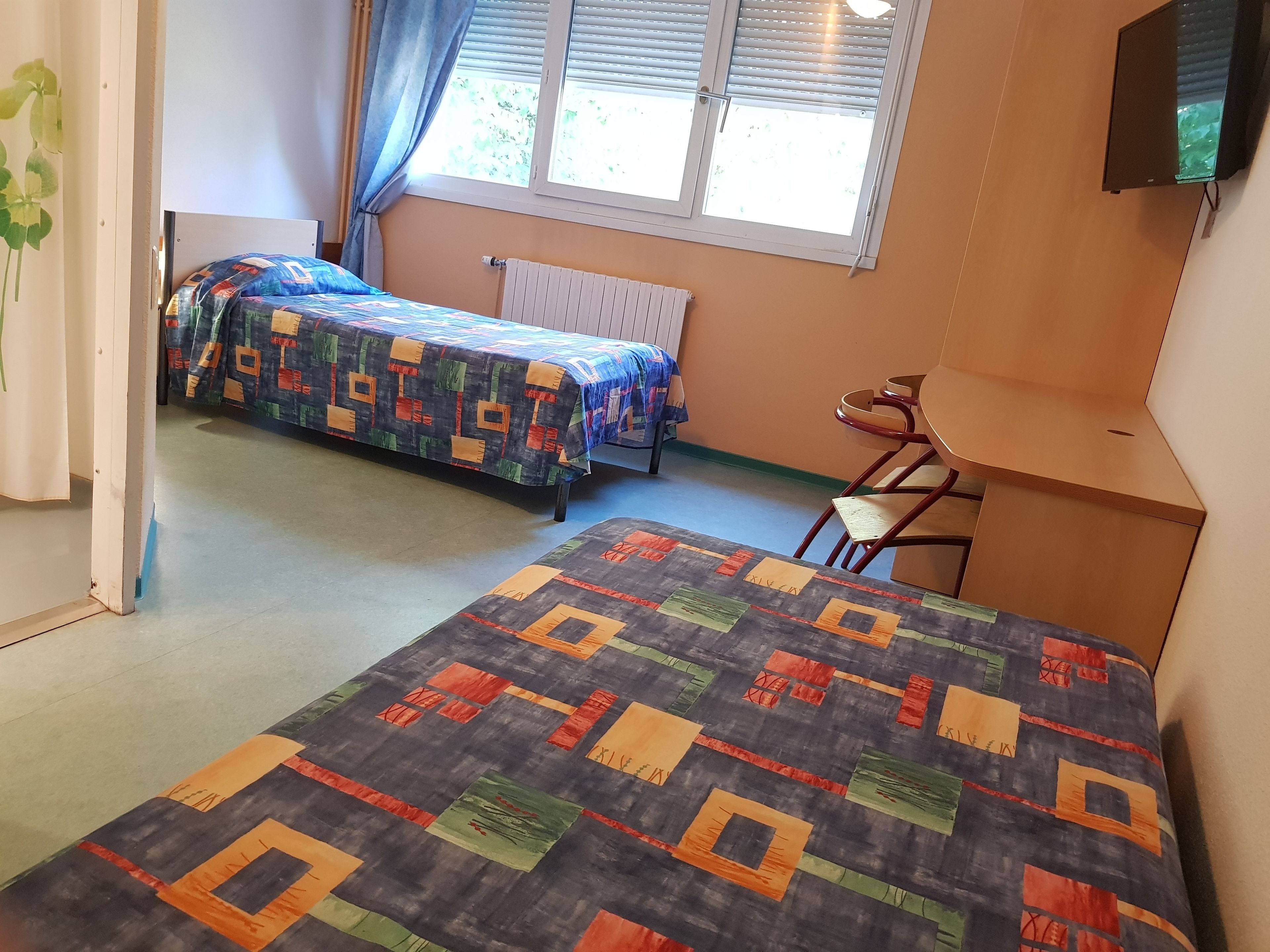 Una habitación con dos camas, una silla, un radiador y una ventana con persianas.