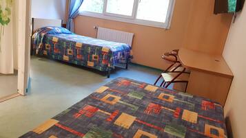Una habitación con dos camas, una silla, un radiador y una ventana con persianas.