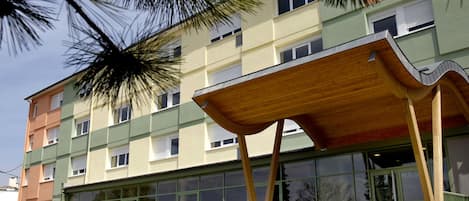 Un edificio de varios pisos con una estructura de madera distintiva en la planta baja, ventanas grandes y una escalera que conduce a la entrada.