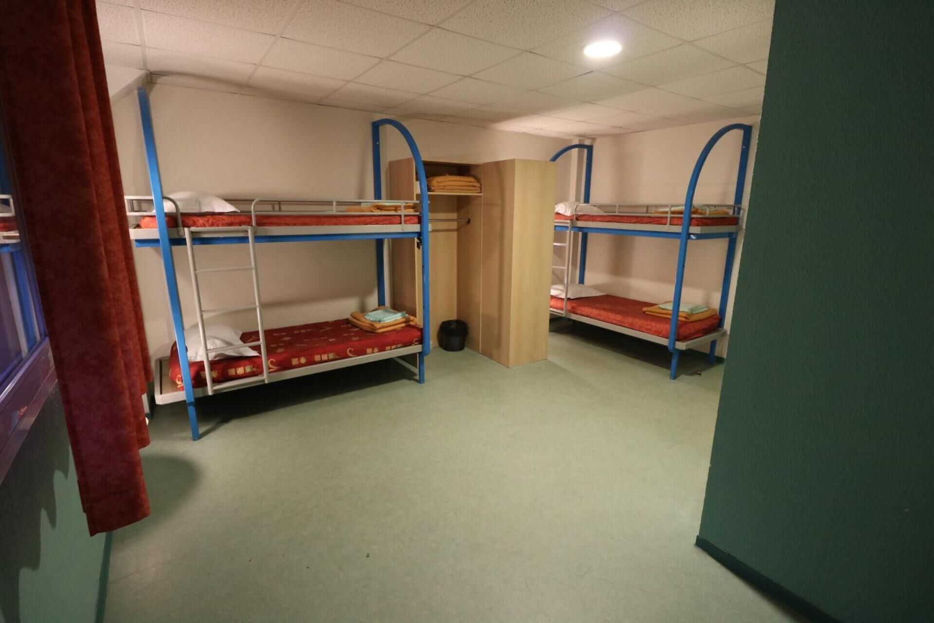A dormitory room with bunk beds, a small closet, and a door leading to another room.