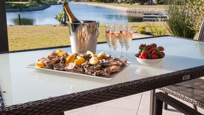 A table with oysters, champagne, and strawberries, overlooking a lake and houses. - Premier Resort The Moorings, Knysna (Knysna)