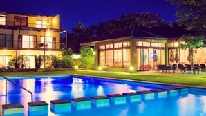 A nighttime view of a modern hotel with a swimming pool, illuminated by ambient lighting. - Premier Resort The Moorings, Knysna (Knysna)