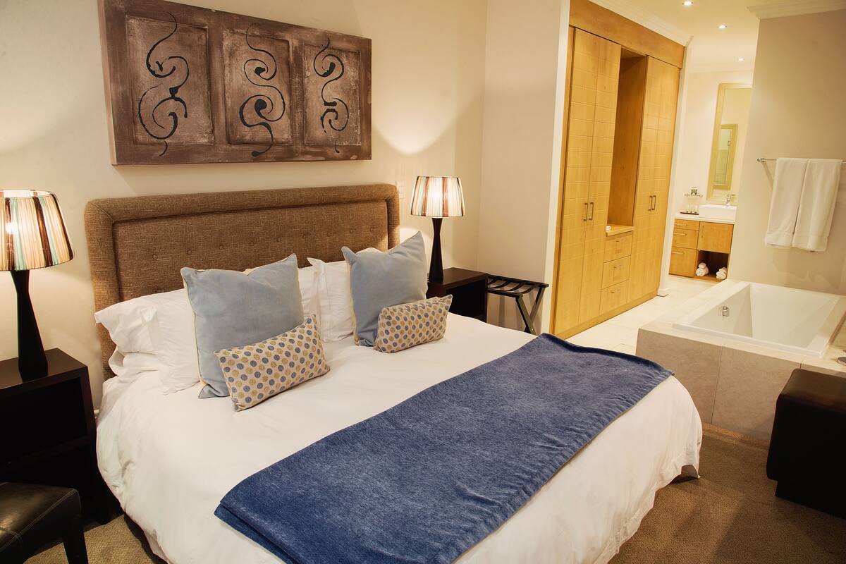 A neatly made bed with a blue blanket, a wooden headboard, and a wall art piece above it.