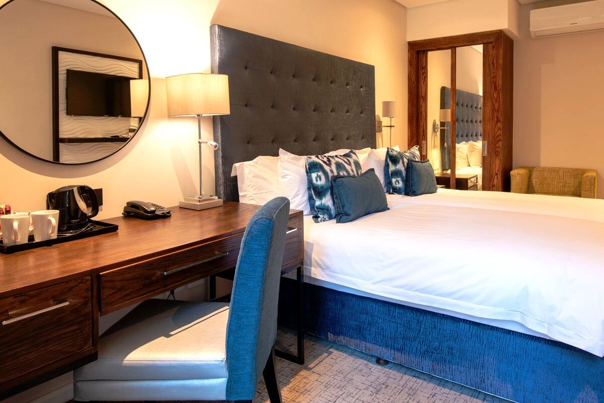 A hotel room with a large bed, a desk with a chair, a TV, and a mirror.