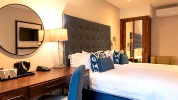 A hotel room with a large bed, a desk with a chair, a TV, and a mirror.