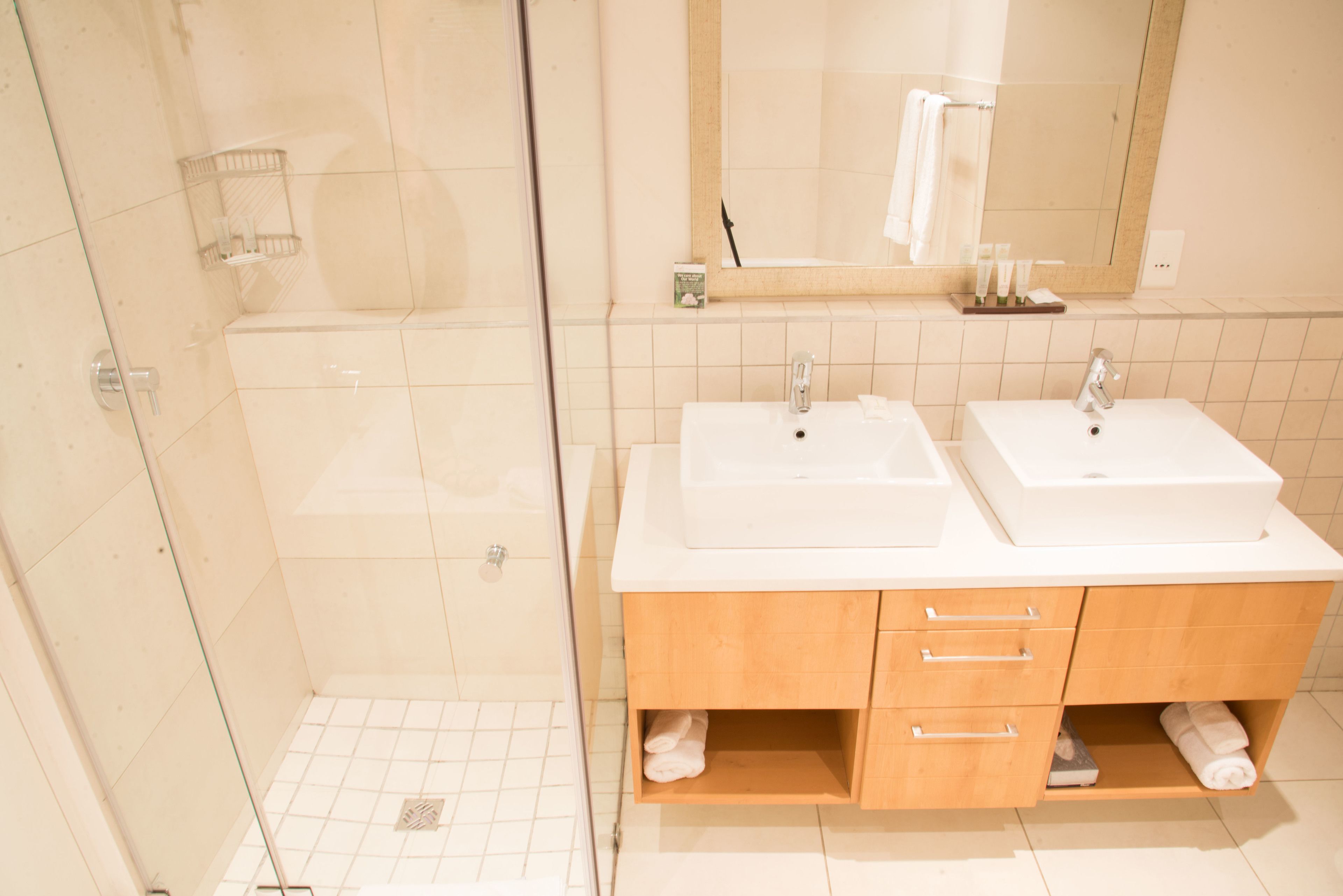 A modern bathroom with two sinks, wooden cabinets, and a glass shower enclosure.