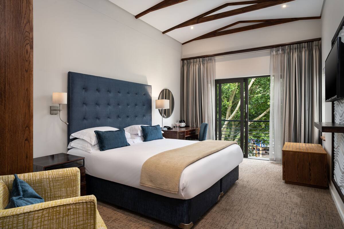 A modern hotel room with a large bed, a wooden nightstand, a desk, a chair, and a television.