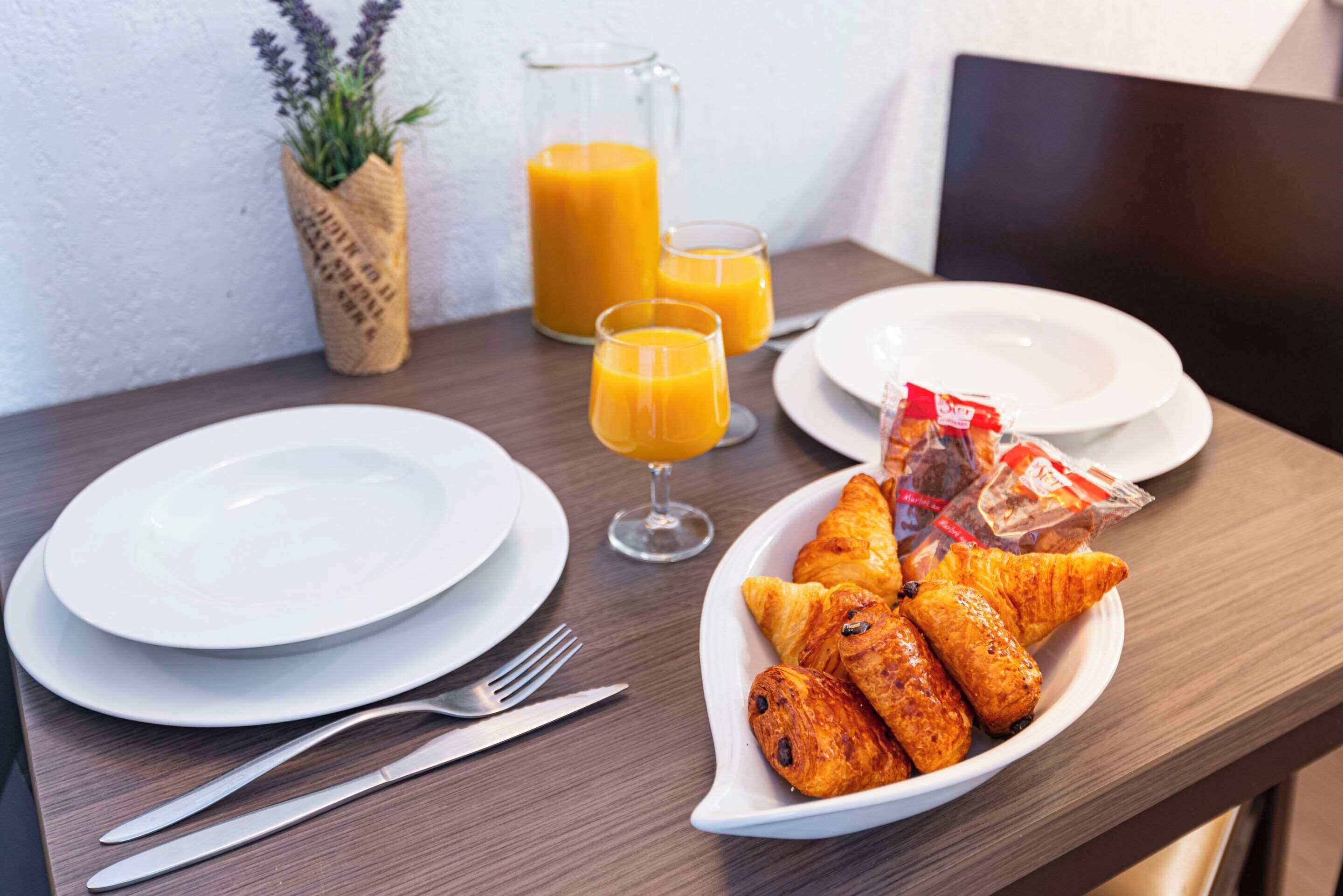 Une table mise pour le petit-déjeuner avec des croissants, du jus d’orange et une petite plante.